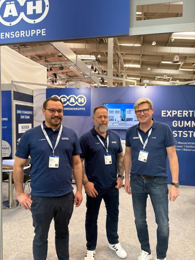 Das Bild zeigt drei Späh-Mitarbeiter in dunkelblauen Poloshirts vor einem Messestand der SPÄH Unternehmensgruppe, der in dunkelblauen und weißen Farben gehalten ist und die Aufschrift "EXPERTEN IN GUMMI & KUNSTSTOFF" trägt.