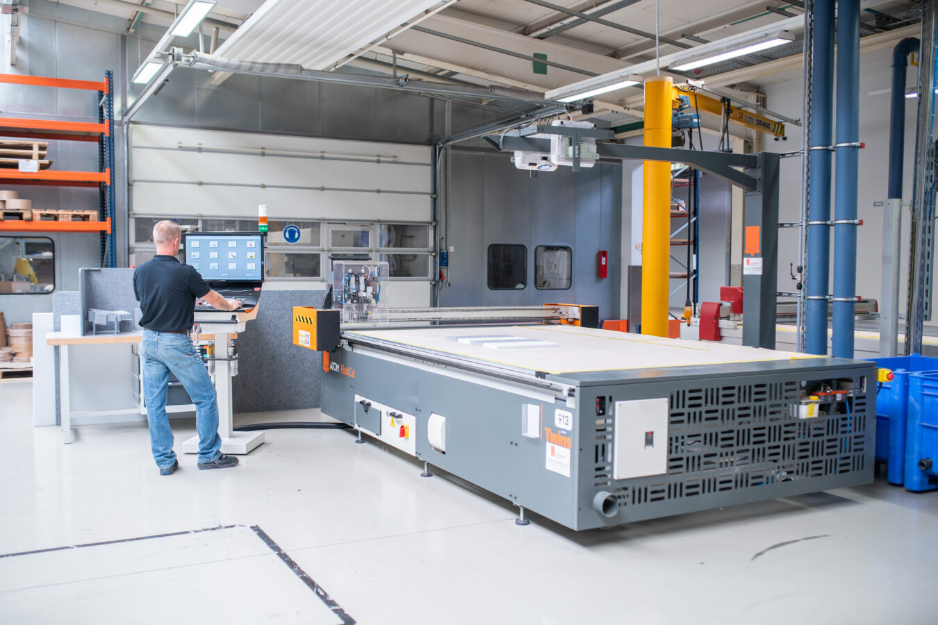 Ein Mitarbeiter bedient das Steuerpult einer großformatigen CNC-Schneideanlage in einer modernen Industriehalle.