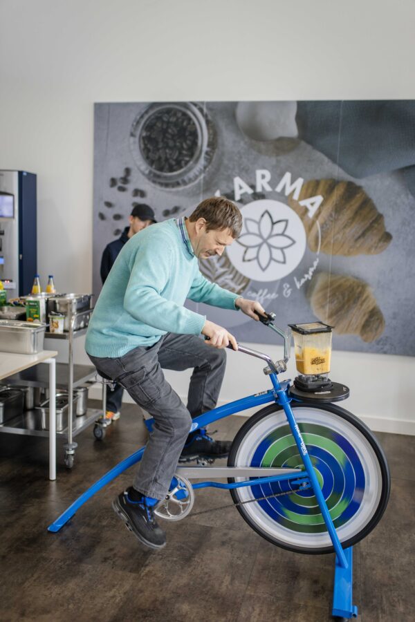 Ein Mann betreibt mit einem speziell umgebauten blauen Fahrrad einen Mixer, um durch Muskelkraft Smoothies zuzubereiten.