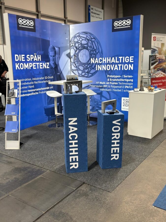 Die Rückwand am Messestand veranschaulicht unter dem Titel „Nachhaltige Innovation“ den Prozess der Ersatzteilfertigung mittels 3D-Druck.