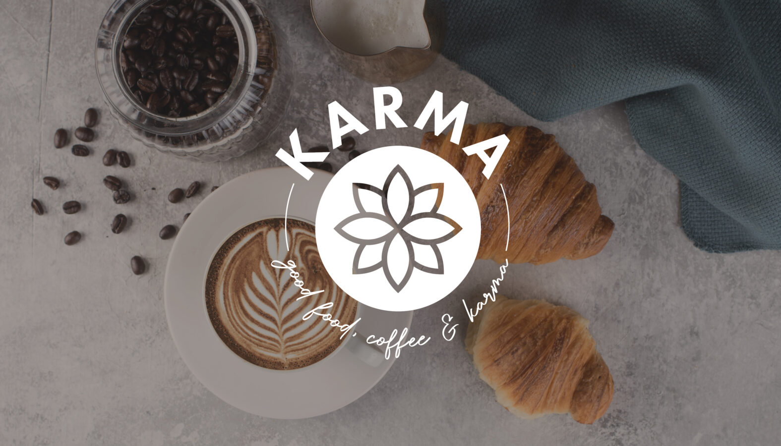 Eine stimmungsvolle Lifestyle-Aufnahme zeigt das Logo von „KARMA – good food, coffee & karma“ inmitten von Kaffeebohnen, Latte Art und Croissants.