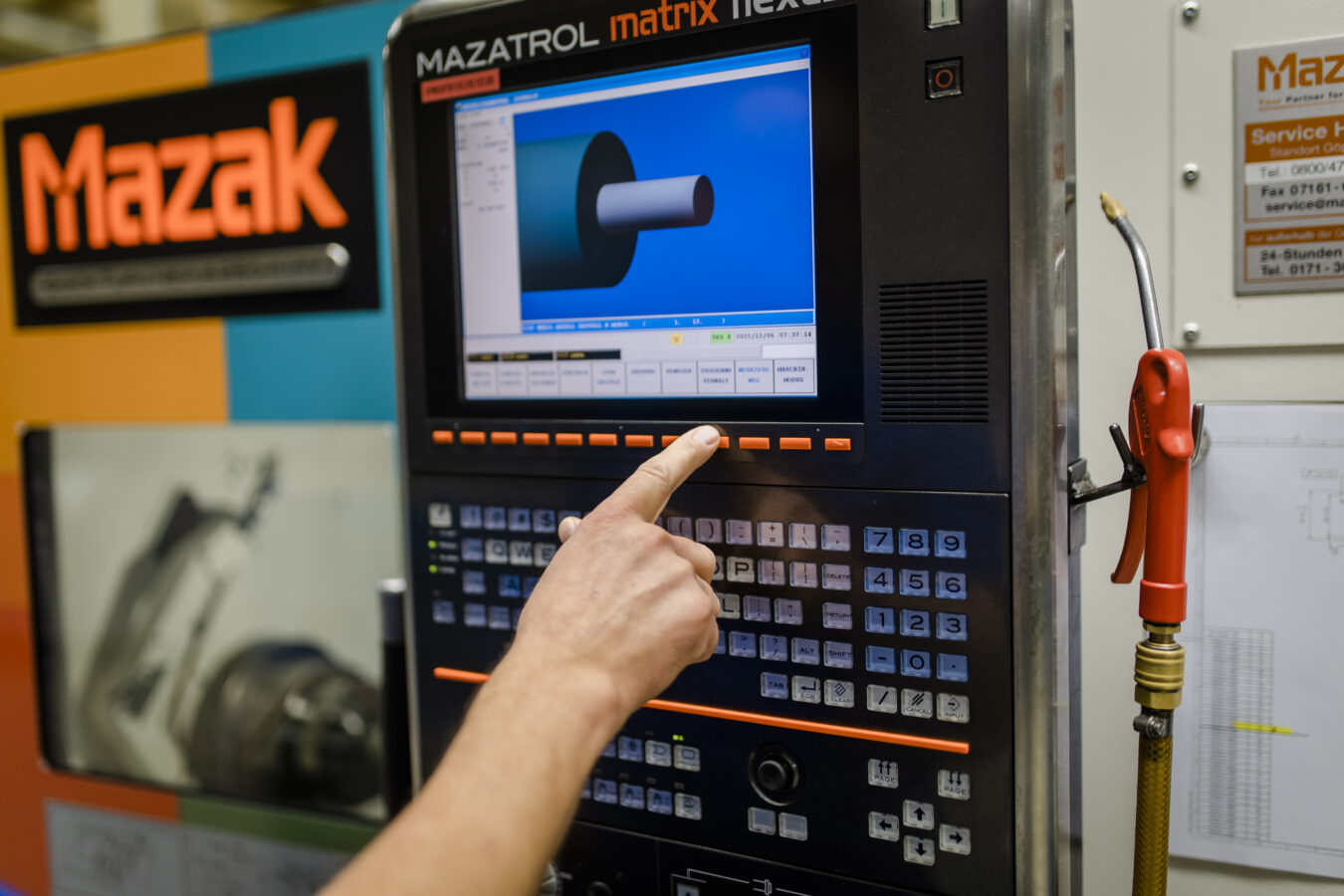 Ein Mitarbeiter bedient das Bedienfeld einer Mazak CNC-Drehmaschine, auf dessen Monitor die digitale Simulation eines Werkstücks zu sehen ist.