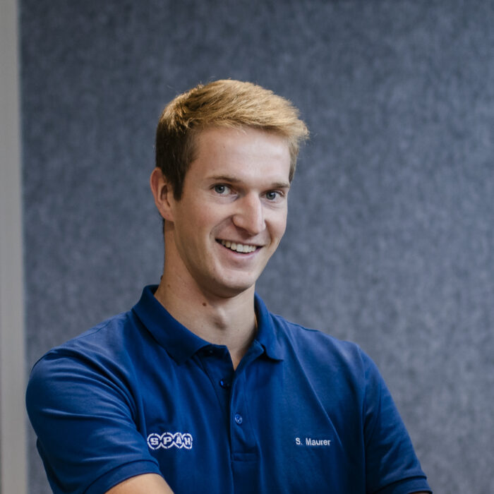 Ein junger, lächelnder Mann in einem blauen Späh-Polohemd mit dem Namensschild 