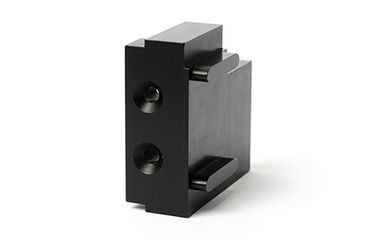 Ein massiver, quaderförmiger Block aus schwarzem Kunststoff mit zwei präzisen Senkbohrungen und seitlichen Führungsstegen liegt als gefertigtes Werkstück auf einem weißen Hintergrund.