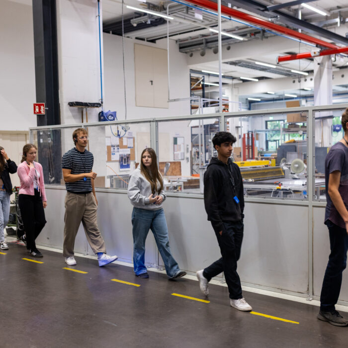 Eine Gruppe von Auszubildenden laufen hintereinander her, in der Produktion von der Firma Späh. Sie hören aufmerksam zu und konzentrieren sich auf das gehen.