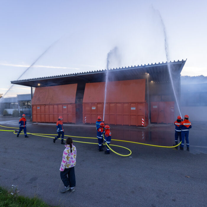 Mehrere Kinder aus der Jugendfeuerwehr geben Strahlen mit den Schläuchen ab auf die Überdachung der Müllcontainer.