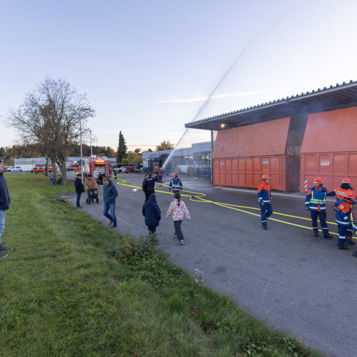 Mehrere Kinder aus der Jugendfeuerwehr geben Strahlen mit den Schläuchen ab auf die Überdachung der Müllcontainer.