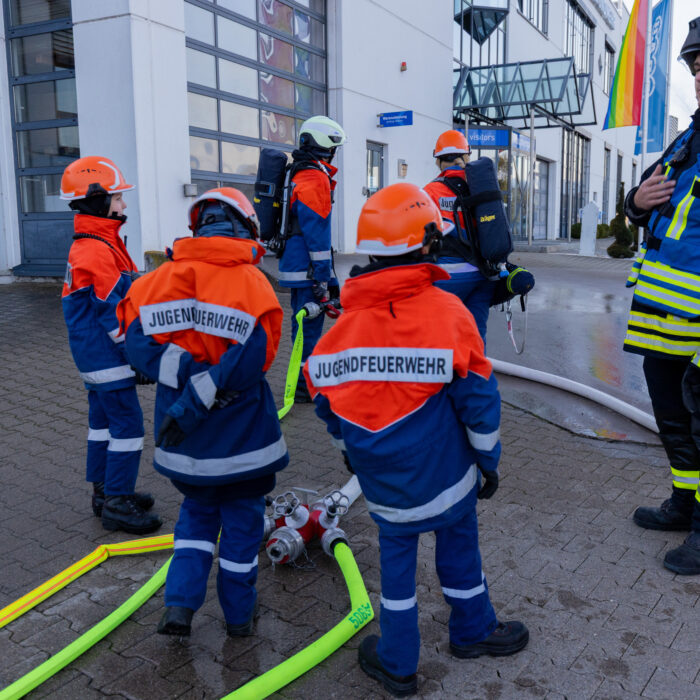 5 Mitarbeiter der Jugendfeuerwehr und ein Mitarbeiter der Feuerwehr stehen vor dem Späh Haupteingang mit den Wasserschläuchen.