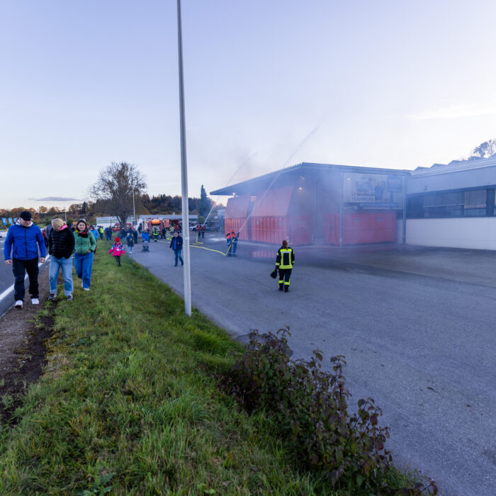 Vier Kinder aus der Jugendfeuerwehr geben mit den Schläuchen zwei Strahlen ab auf die Überdachung der Müllcontainer.