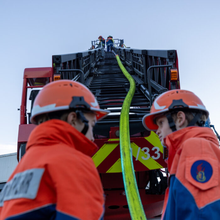 Zwei Kinder von der Jugendfeuerwehr stehen unterhalb der Drehleiter. Die anderen beiden Kinder sind im Korb der Drehleiter mit einem Löschschlauch.