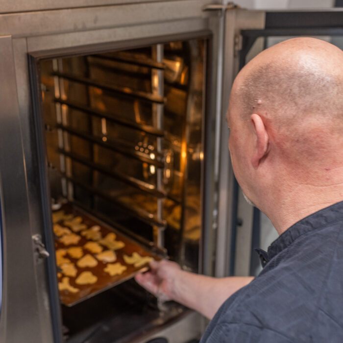 Der Koch schiebt ein volles Backblech mit Weihnachtsgebäck in den leicht erhitzten Ofen.