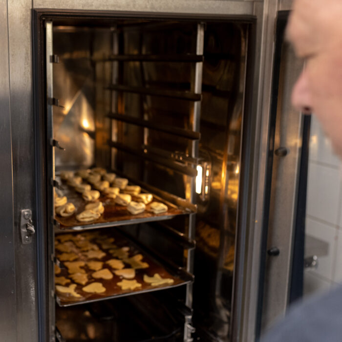 Zwei volle Backbleche mit Weihnachtsgebäck sind im leicht erhitzten Ofen. Der Koch macht die Tür des Ofens zu.